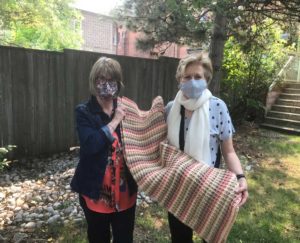 Giselle Weaver (L) giving one of six blankets to Melodie Pritchard (R). Although their smiles are concealed, the gift of loving care speaks loudly as they hold one of seven lap blankets made by Giselle.